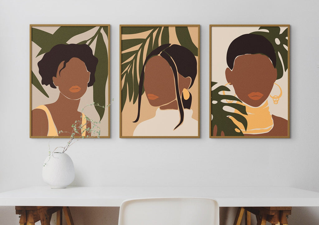 Three "Beautiful African Women" prints by Wall Funk hang above a white table with a round vase, featuring abstract floral designs.